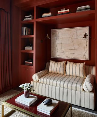 home office painted in burgundy with wall to wall shelving and a striped sofa