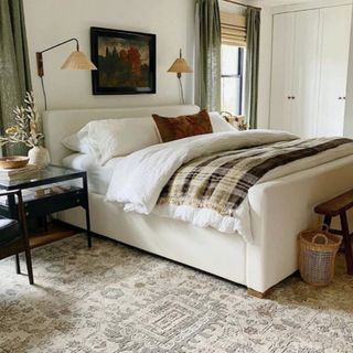 An example of how to design a bedroom showing a bedroom with neutral colour scheme, hardwood floor, a rug and wall lights