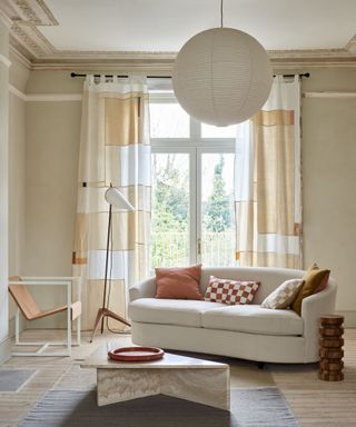 Modern cream living room with abstract printed curtains, curved sofa, rug, coffee table, lantern pendant