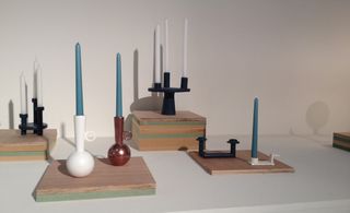 White floor and wall, wooden layered colour blocks, white, black and brown candle holders with blue and white candles