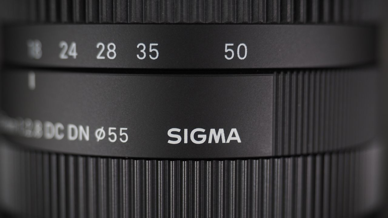 The Sigma 18-50mm f/2.8 DC DN | C Canon RF lens on a wooden surface against a dark background with moody lighting