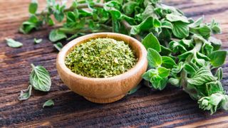 Bowl of dried oregano with fresh oregano lying beside it