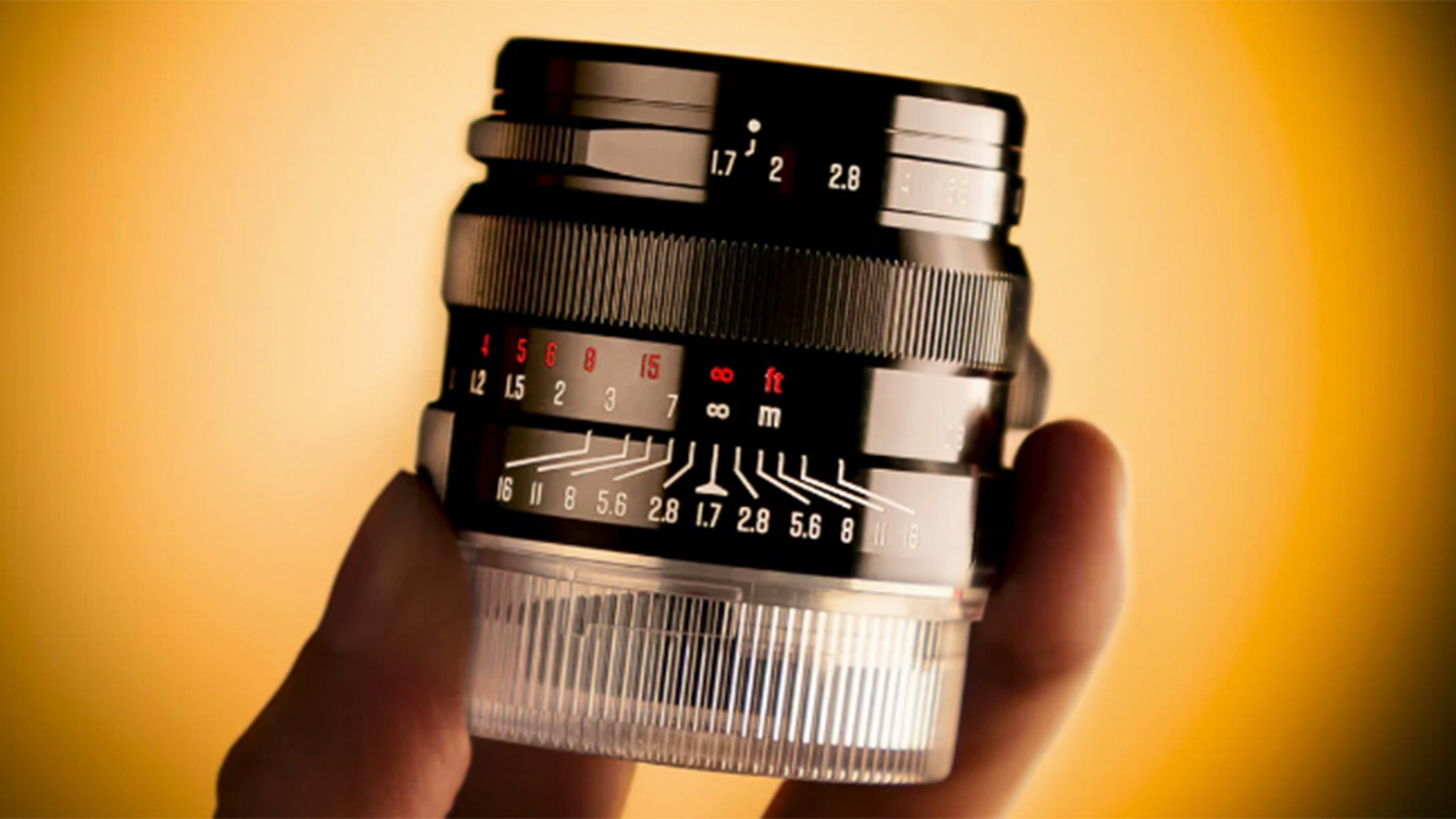 A black camera lens held up with a finger and thumb.