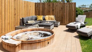 Timber fence surrounding a modern decked area with a hot tub, outdoor sofa and two garden loungers