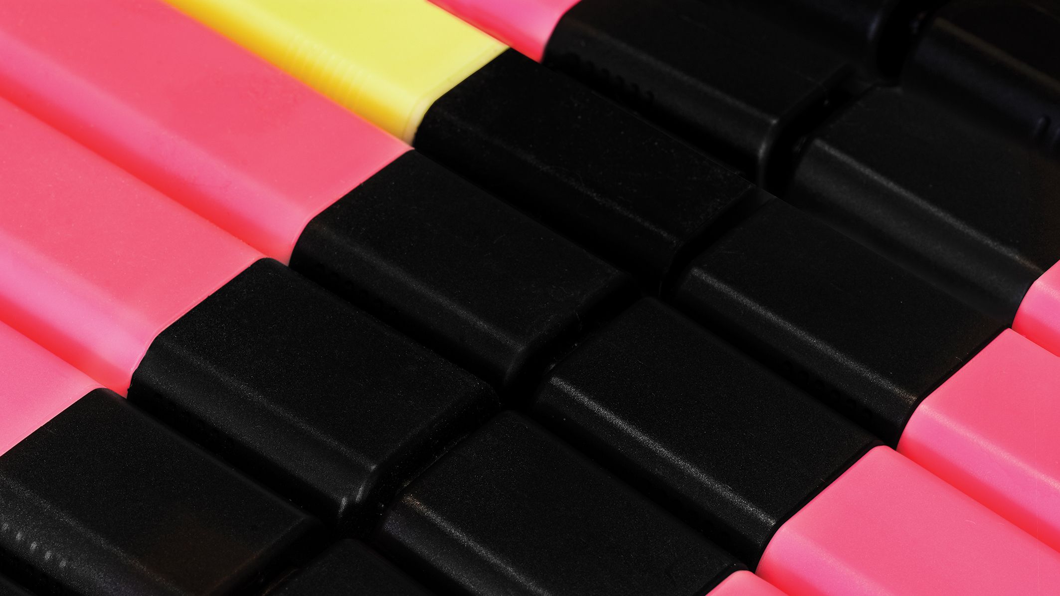 A close-up view of pink and black highlighter caps arranged neatly, with a yellow cap peeking out among them