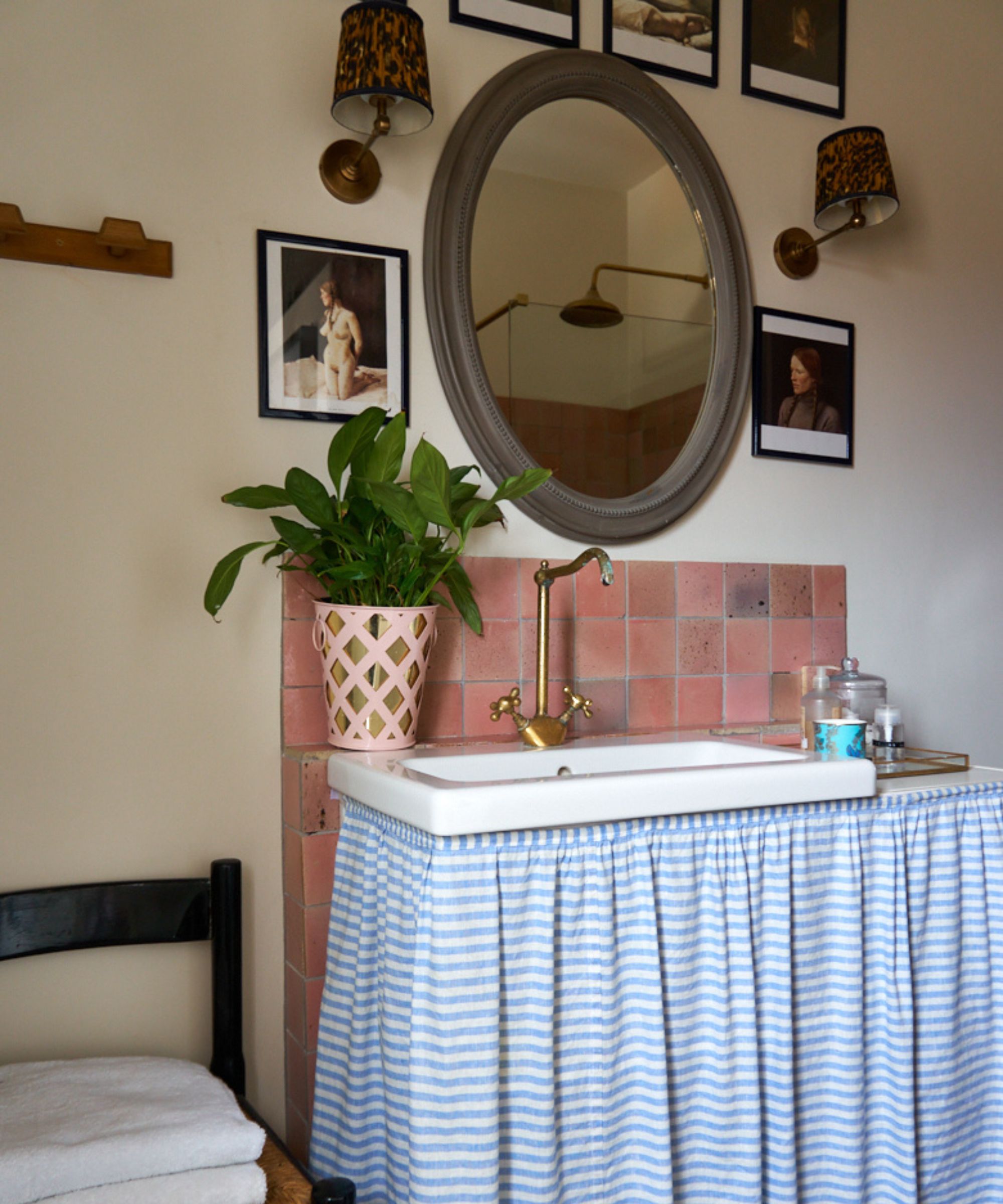 A small bathroom vanity with a blue and white striped cabinet skirt and pink square backsplash tiles