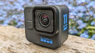 GoPro Hero 11 Black Mini on a wooden plank with blue flowers in the background