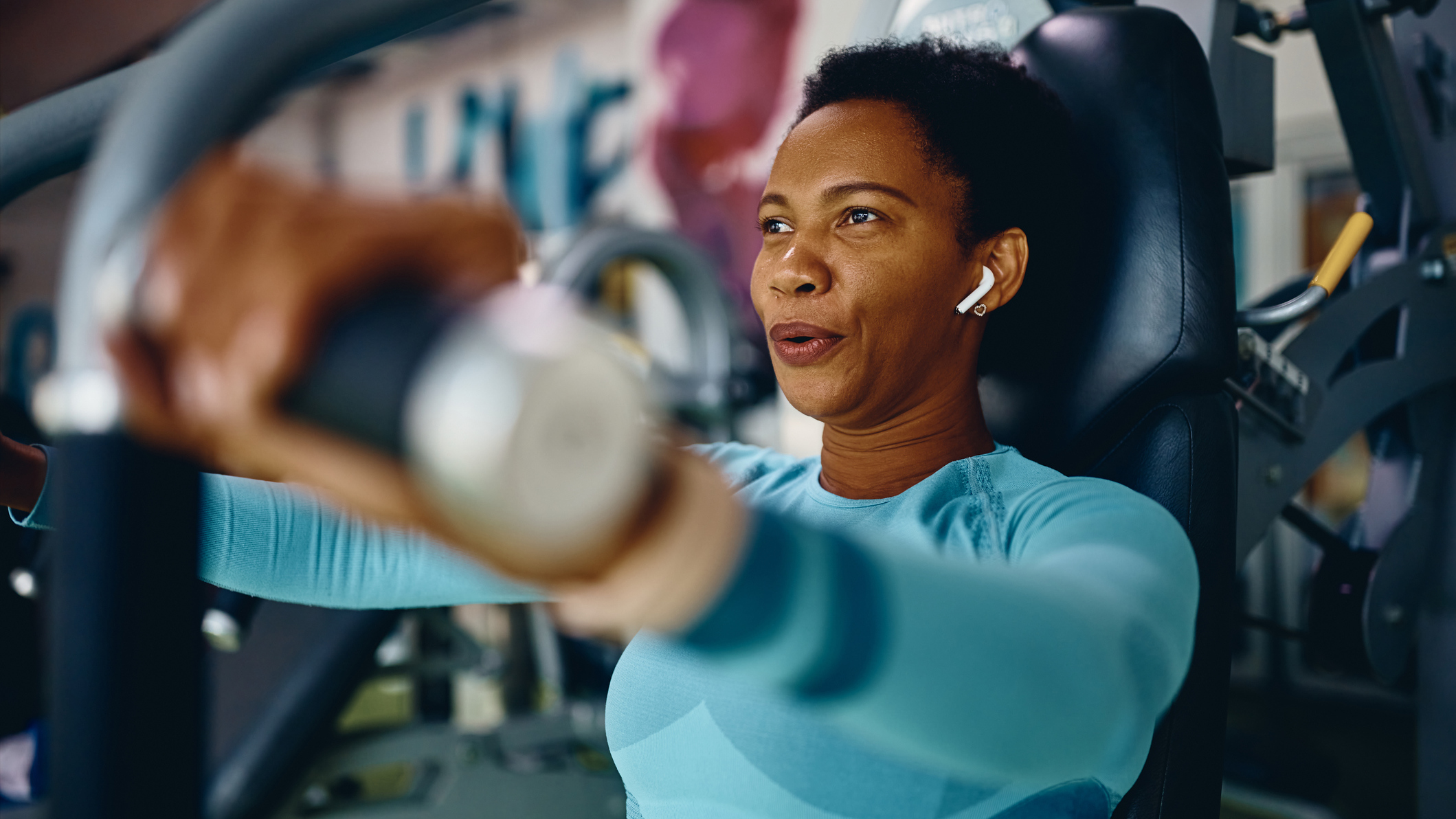 Woman exercising using gym machine, she is pressing the handles of the machine away from her