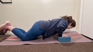 woman performing a push up from her knees with one hand on a yoga block