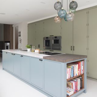 A modern kitchen with light blue kitchen island, light olive green cabinetry and multicolored statment glass light fixture