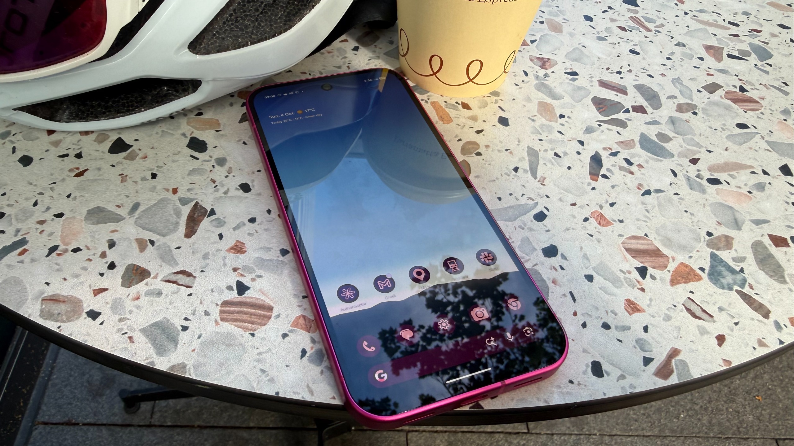 A Google Pixel 11 on a table next to a coffee cup and a bike helmet