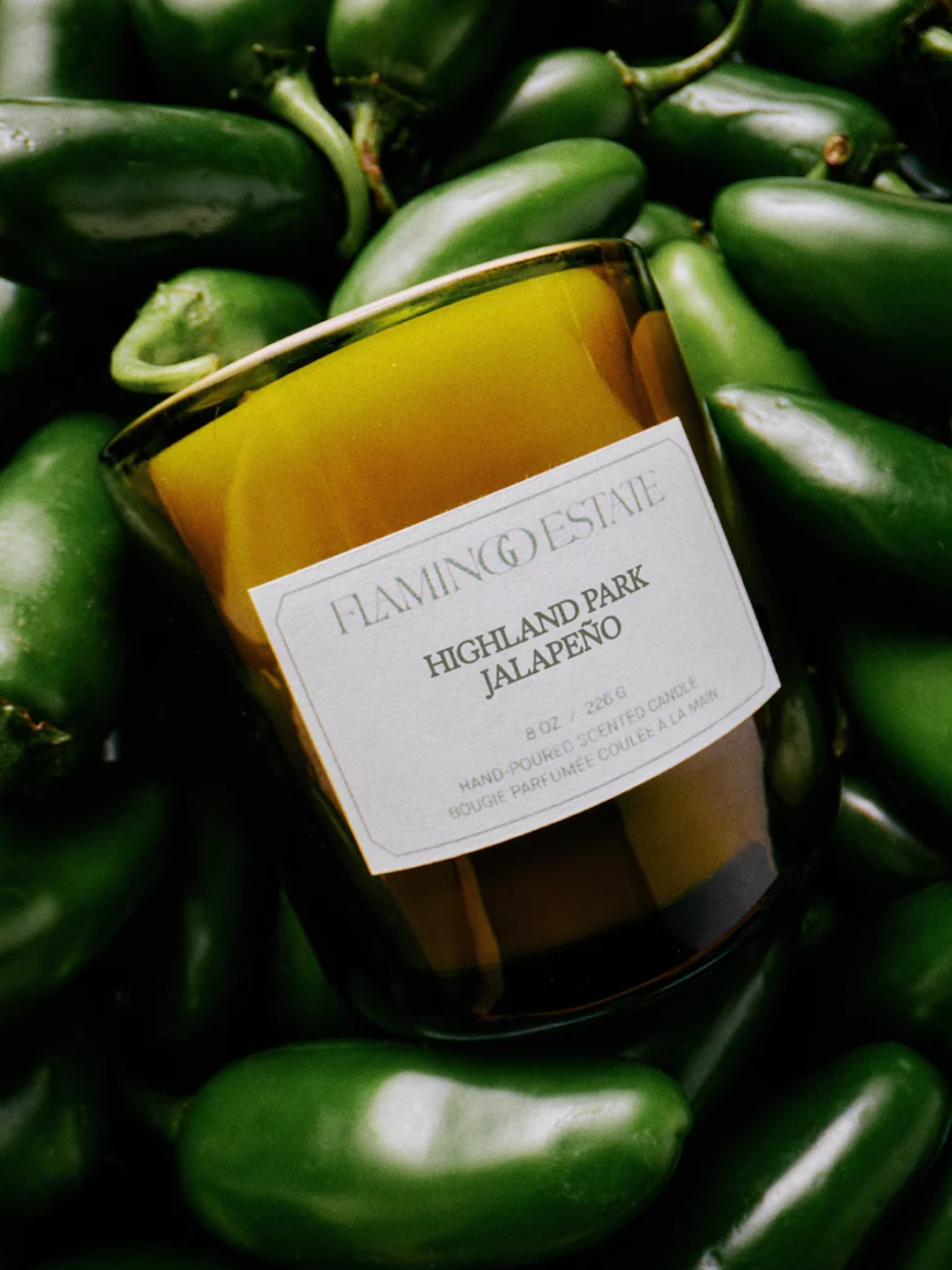A green glass candle from Flamingo Estate in a heap of jalapenos
