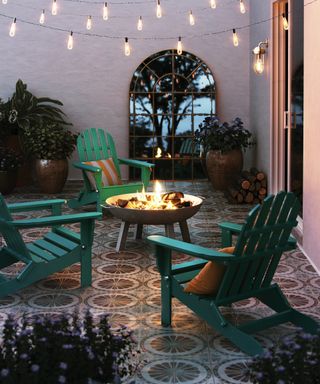An outdoor lounging space with tiled outdoor floor decor, green adironack chairs, black fire pit and arched outdoor mirror decor