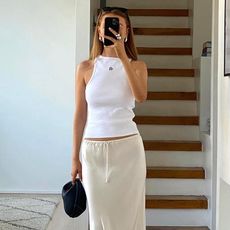female fashion influencer Orlaith Melia poses for a mirror selfie wearing chunky silver earrings and ring, a high-neck white tank top, mini black bag, and cream drawstring slip skirt