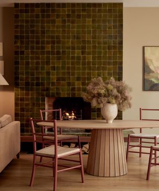 green zellige tiled fireplace chimney breast in a small dining room with red chairs