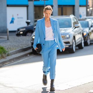 A guest is seen wearing blue suit, white shirt, black bag, Dr Martens boots outside Dsquared during the Milan Fashion Week Fall/Winter 2022/2023 on February 27, 2022 in Milan, Italy.