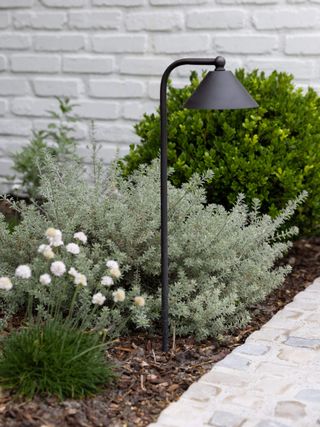 a black pathway light in the border beside a stone paved path