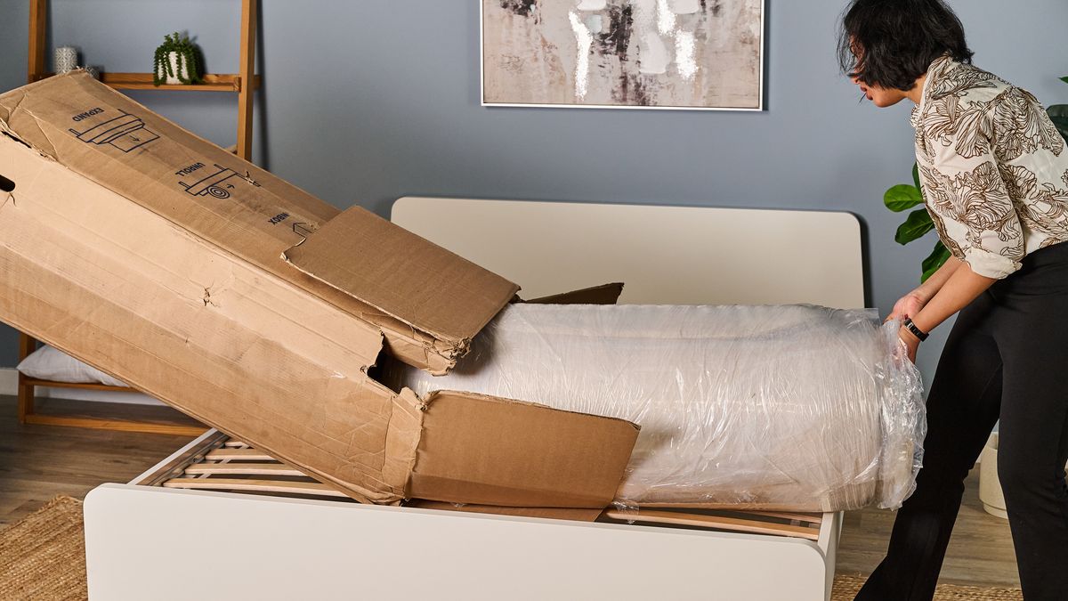 The Birch Luxe Natural mattress rolled up in plastic coming out of its box as a Tom's Guide tester starts to unwrap it