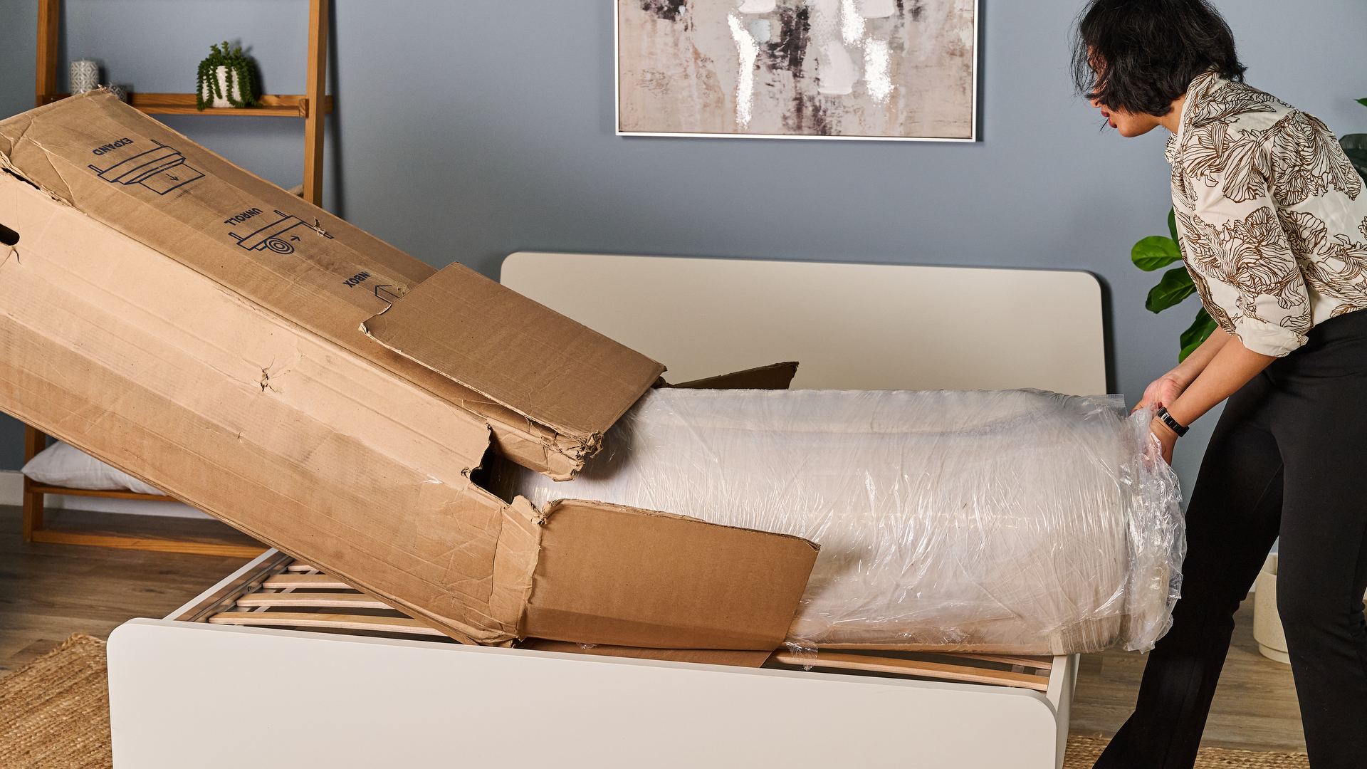 The Birch Luxe Natural mattress rolled up in plastic coming out of its box as a Tom's Guide tester starts to unwrap it