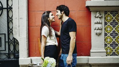 a couple about to embrace while outside next to a brick wall