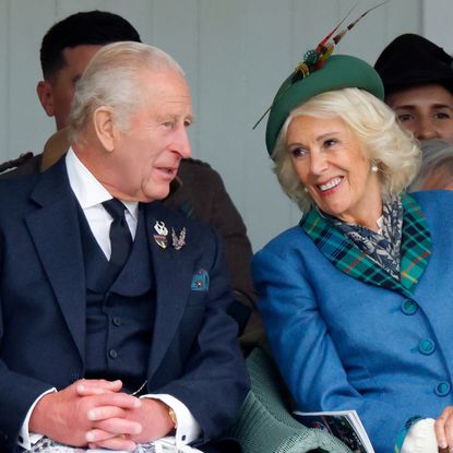 King Charles and Queen Camilla smiling at each other sitting in chairs