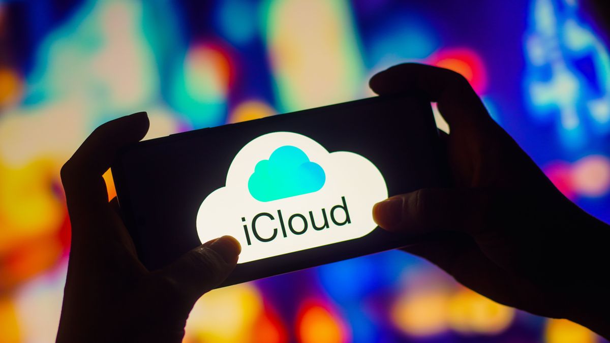 iCloud logo appearing on a smartphone being held in outstretched arms by a silhouetted person against a multicoloured background