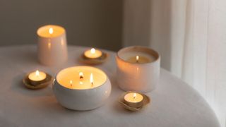 Scented candles in ceramic bowls on linen tablecloth at home. - stock photo