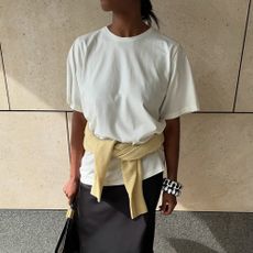 a woman wearing a white tee, black satin skirt, and tan sweater 