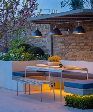 A covered seating area in a garden with 3 overhead pendant lights and under seat heating