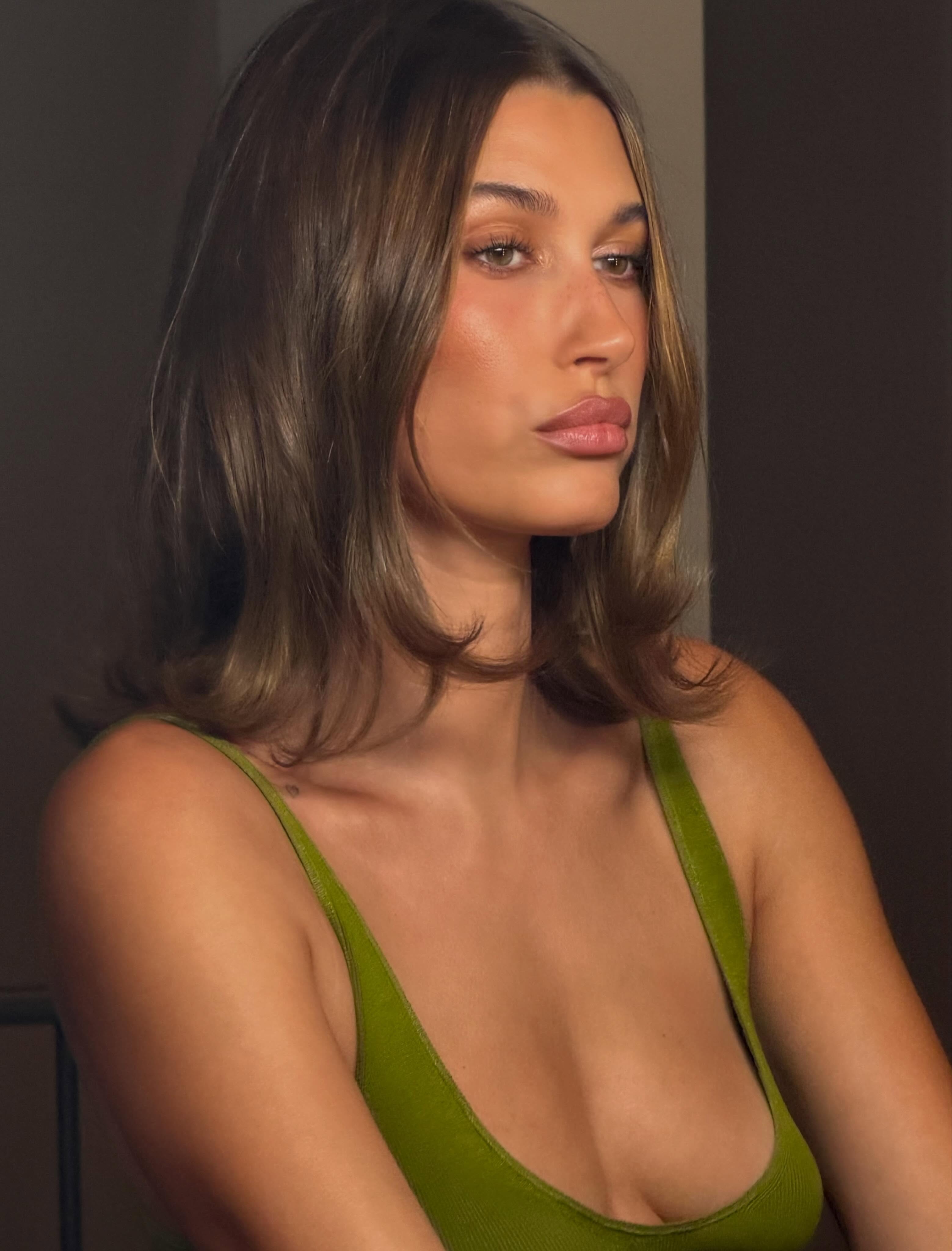 Hailey Bieber with taupe brown hair and caramel highlights.