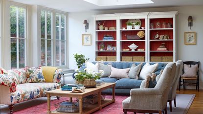 living room with blue sofa floral sofa and grey armchairs with white display shelving with red paneling and rooflight above