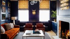 Cozy sitting room with fire lit, dark walls and orange velvet sofa