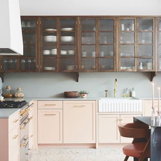 kitchen with white cooker hood and white walls above wall units, pale blue worktops and splash back, butler sink, pale pink units, terrazzo floor, table and chair to side