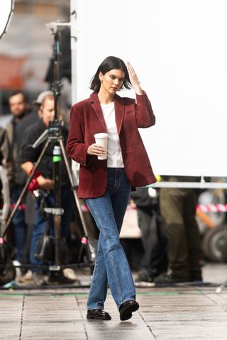 Kendall Jenner wears blue jeans, affordable loafers, red wine suede jacket and a white tee as she carries a coffee cup