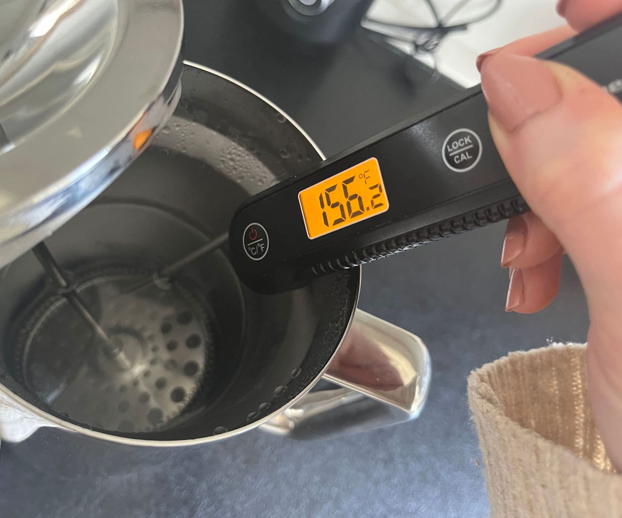 a digital thermometer reading the temperature of water in a stainless steel coffee press. It shows 156F