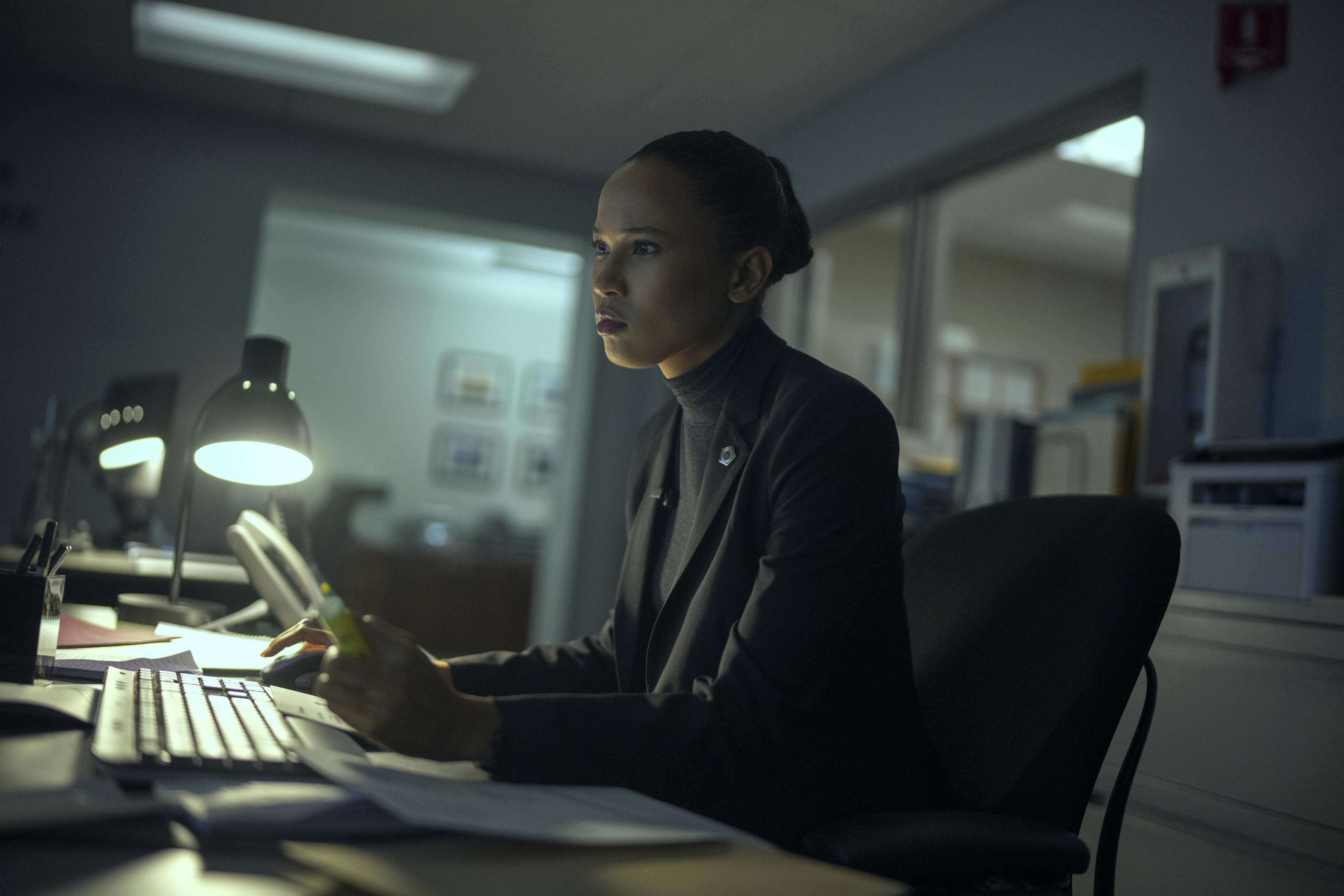 fola Evans-Akingbola as Chelsea Arrington sitting in a dark office at a dimly lit computer typing on the keyboard in a still from the night agent season 3