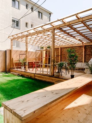 large wooden pergola covers wooden decking area, next to patch of grass