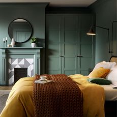 A bedroom with green fitted wardrobes and a fireplace