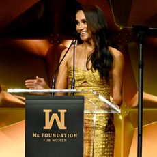 Meghan Markle in a gold gown speaking behind a podium
