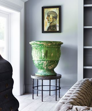 Large green sculpture on black pedestal, small artwork hung above on wall, blue-gray painted walls