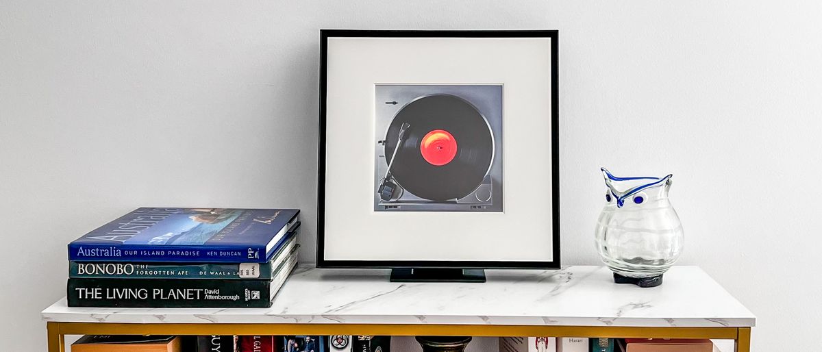 Samsung Music Frame on a table beside some books and a vase