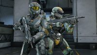 Two Spartan soldiers stand back-to-back in Halo Infinite, holding rifles inside a futuristic facility.