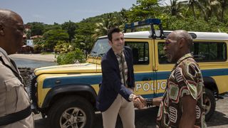DI Neville Parker (Ralf Little) shakes hands with Dwayne Myers (Danny John-Jules), who is still in his casual clothes of a brightly-patterned brown shirt, while the Commissioner (Don Warrington) looks on