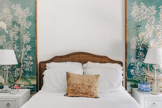 green and white bedroom with green chinoiserie panels each side above the bed, French style rattan bed, white bedding, vintage cushion, white side tables and white and glass tables lamps