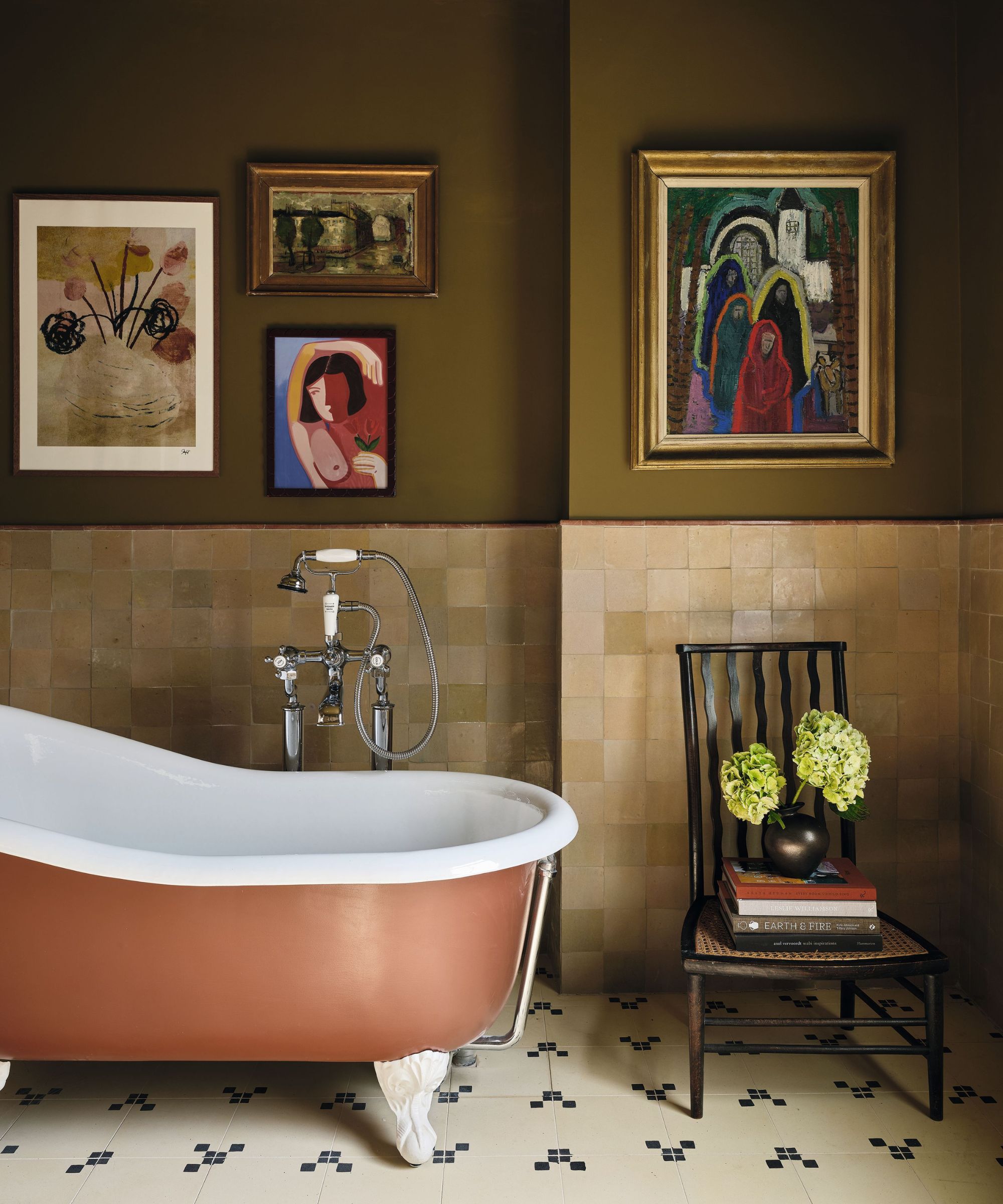an earthy olive green bathroom with a rust orange bath tub and modern artwork