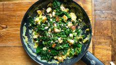 Black frying pan filled with green veg, scrambled eggs and cubes of halloumi on wooden table