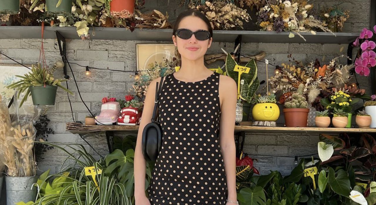 Olivia Rodrigo wears a polka dot Reformation dress standing in front of a flower stand