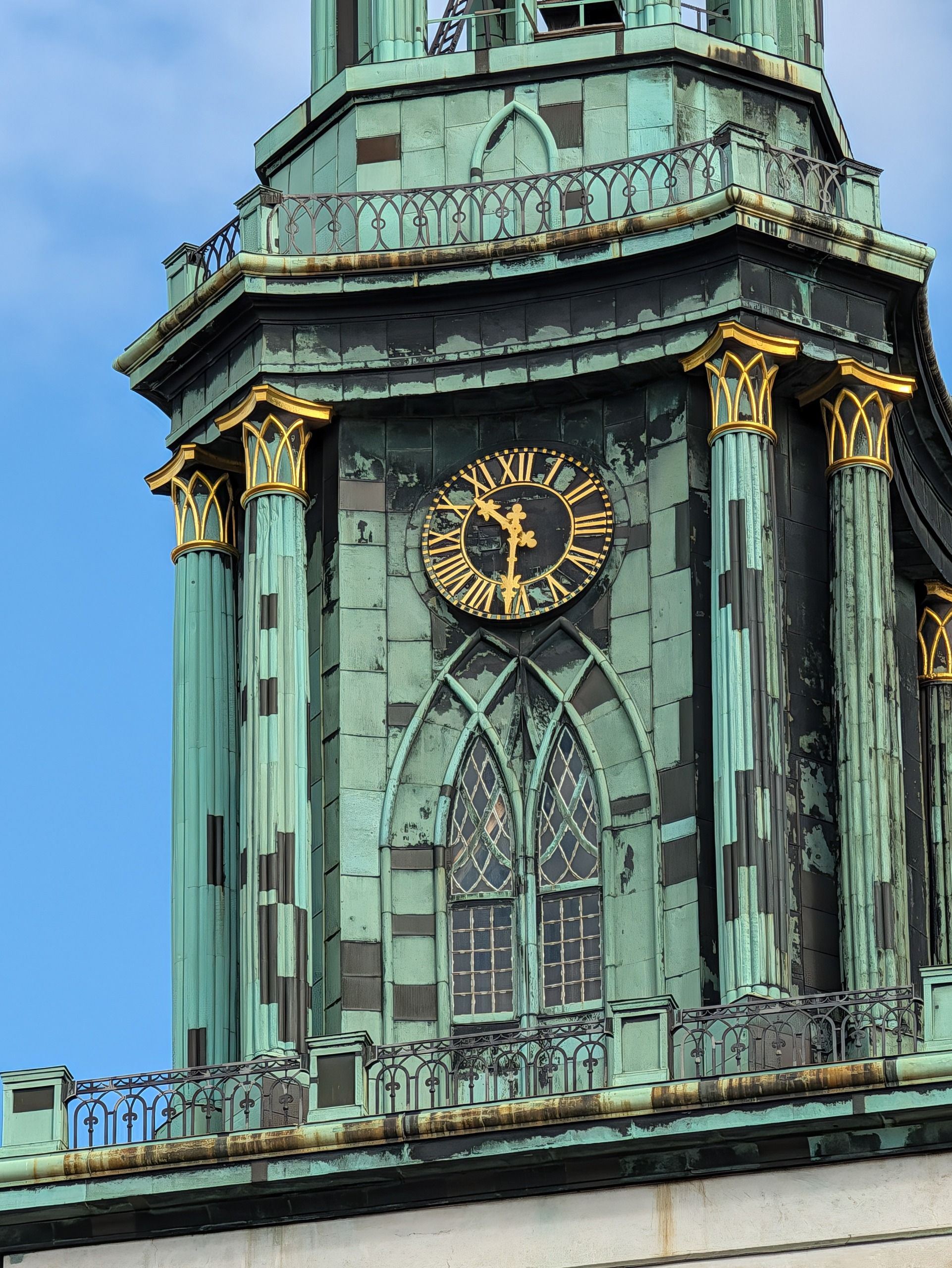 Close-up of a gold clock face and weathered green copper detailing on a historic church tower.