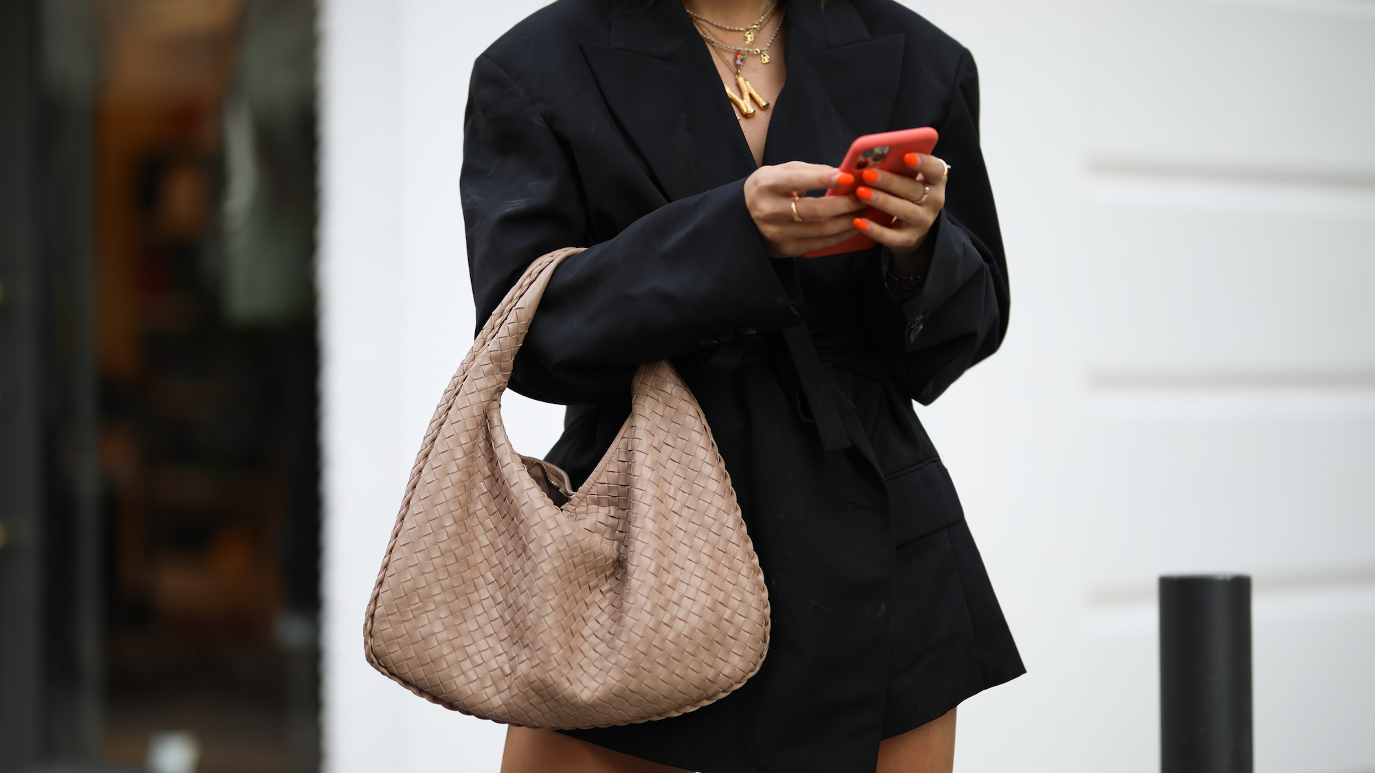 Woman wearing black blazer dress, gold jewellery, Bottega bag and bright orange nail colour to make tan pop
