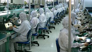 Workers in protective suits seated in rows at a smartphone assembly facility